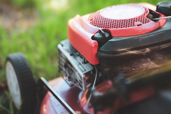 A bright red lawn mower resting on a vibrant green field, capturing the fresh, well‑kept look Hedgie