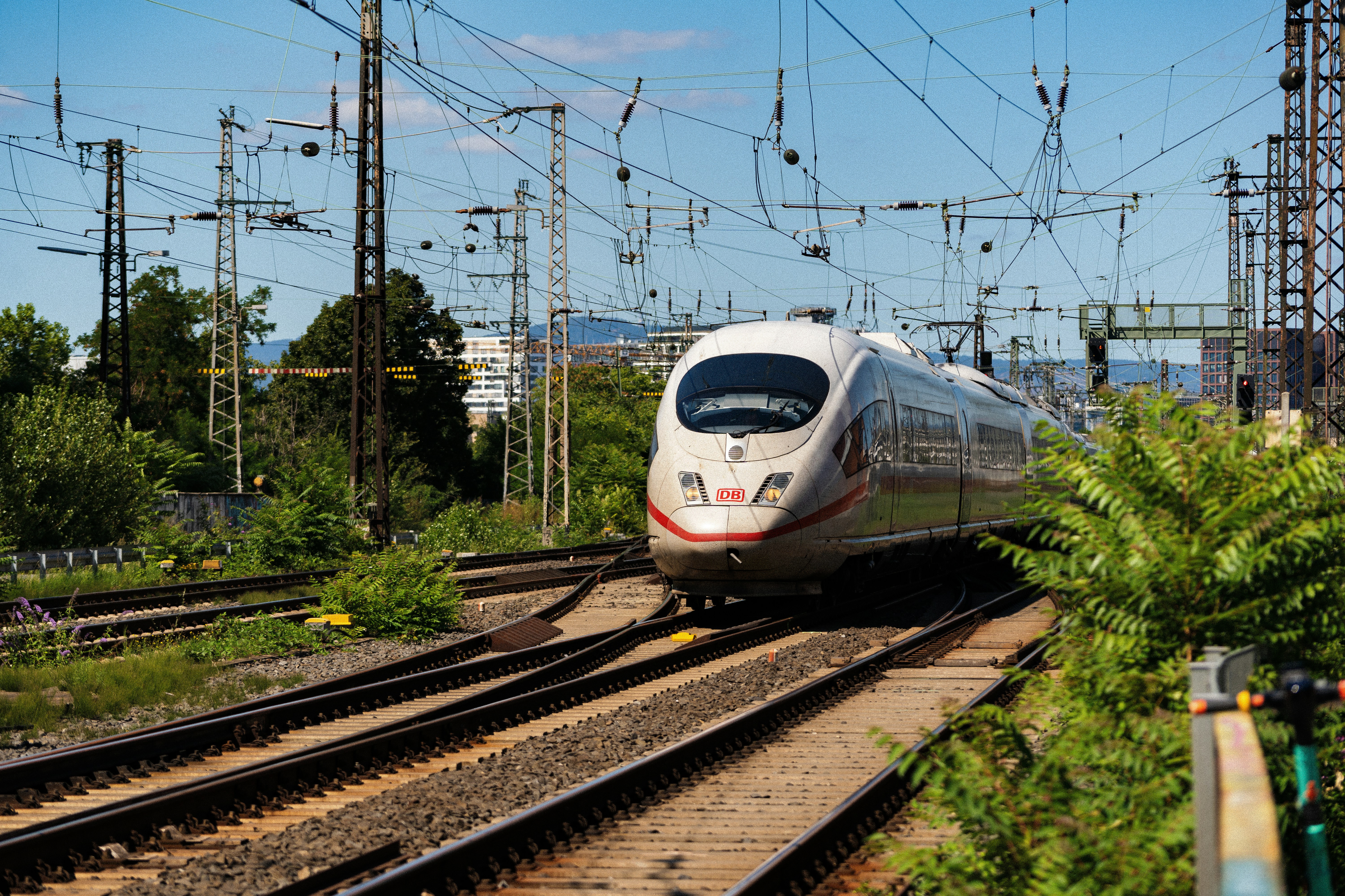 A white train traveling down train tracks next to a forest, ICE 3 High Speed Train Exiting Frankfurt Main Station