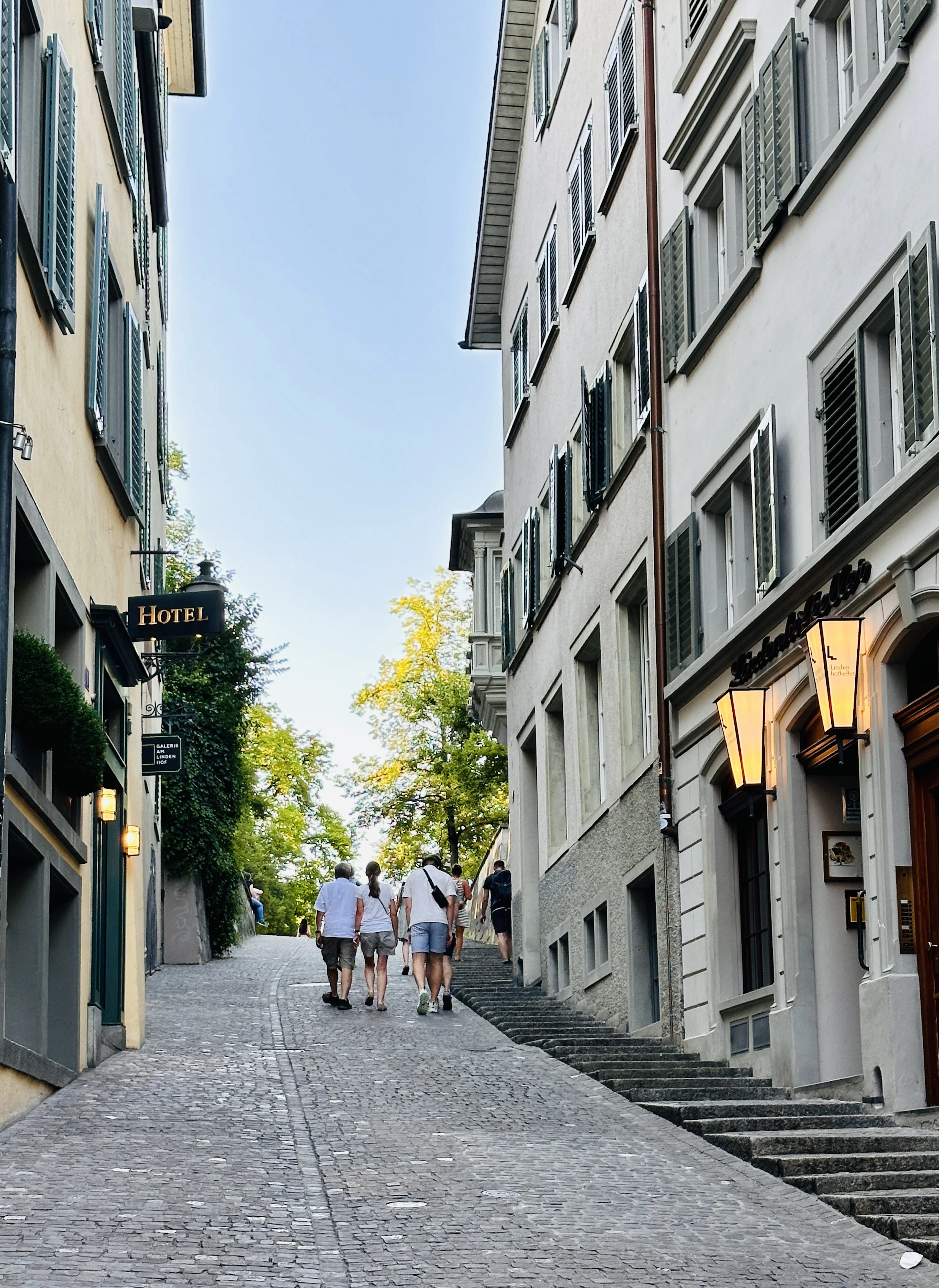 Visitors climb a cobblestone lane past a lantern and a hotel sign on the way up to Lindenhof.