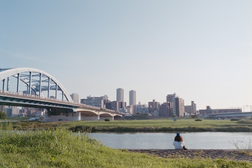 A person sitting on a bench near a river and a bridge