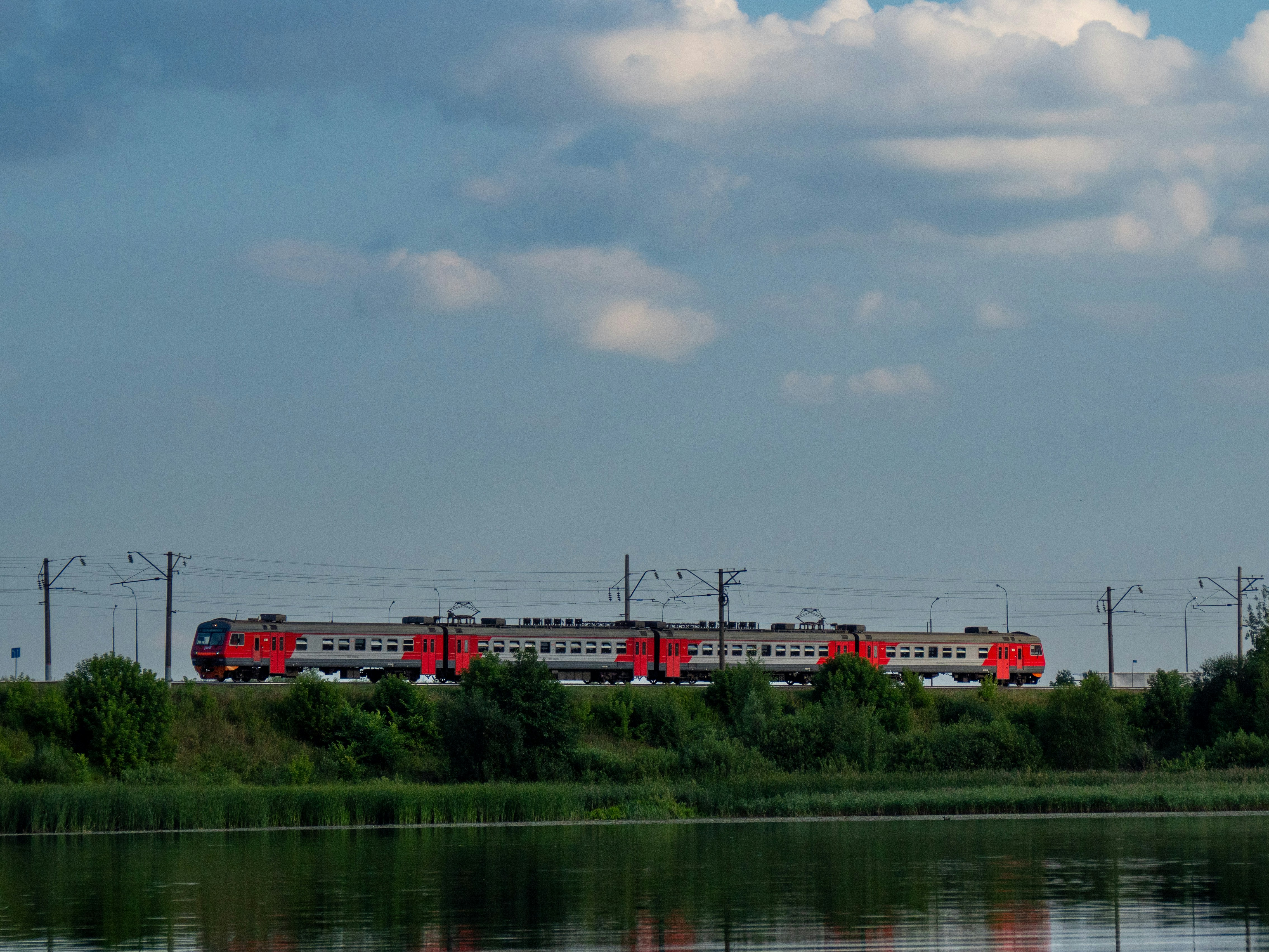 A red train traveling down tracks next to a body of water