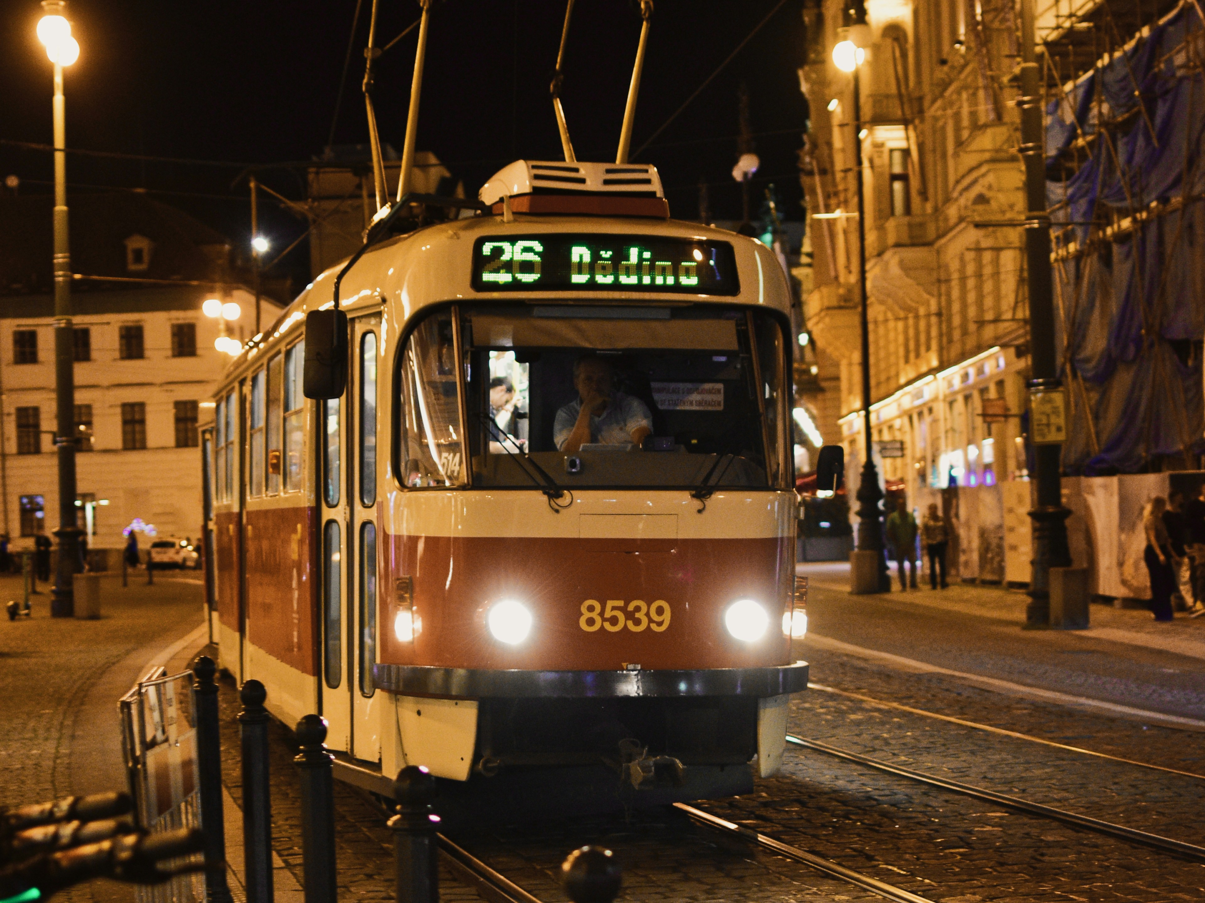 Pražská tramvaj s rozsvícenými světly projíždí večerní ulicí