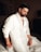 A man sitting on top of a bed in a white suit