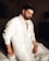 A man sitting on top of a bed in a white suit