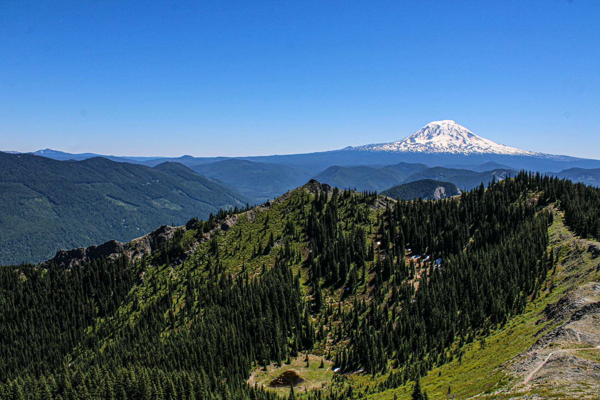 A view of a mountain range with a snow capped mountain in the distance