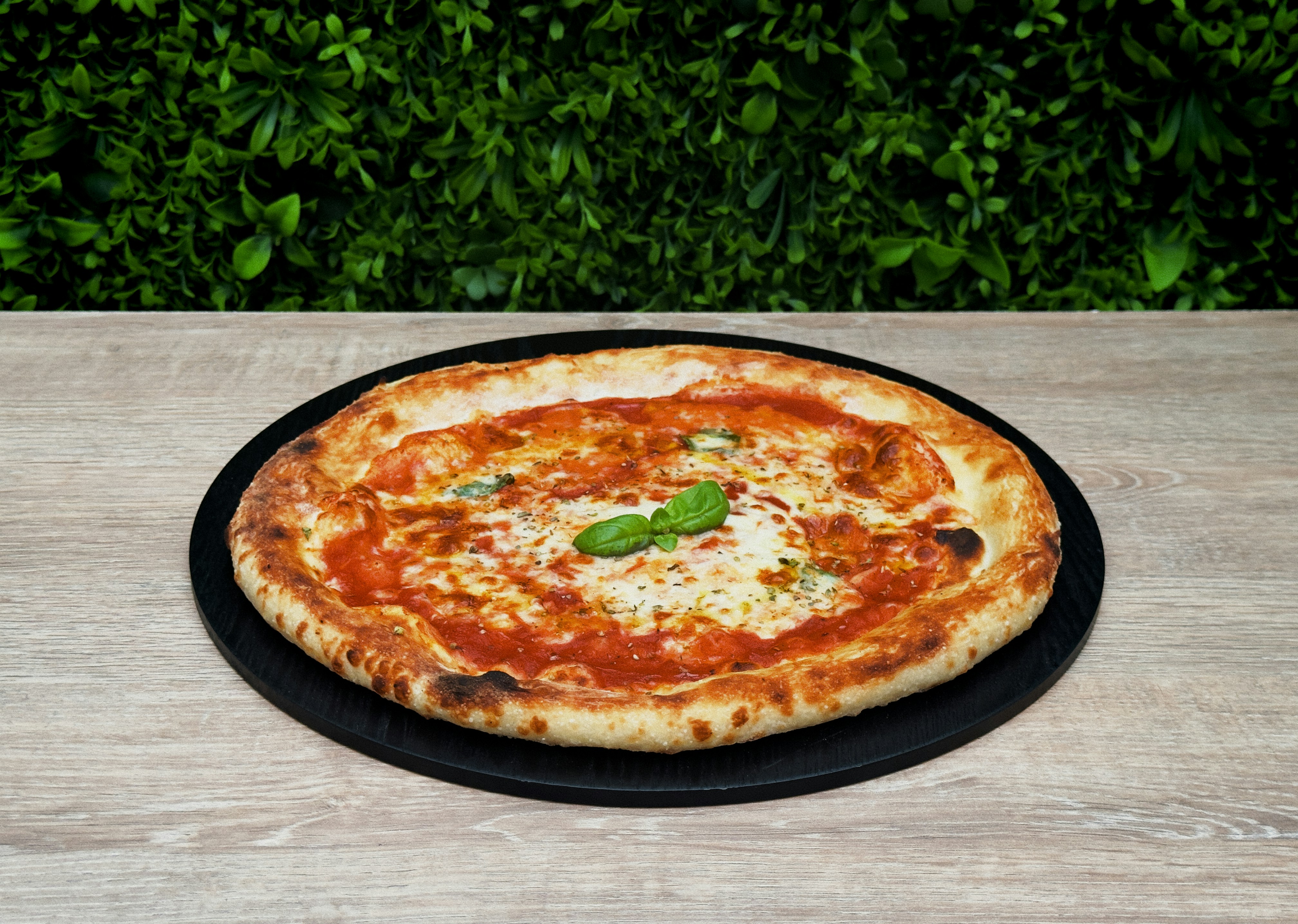 Una pizza margherita fresca su un tagliere di legno nero.