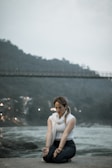 A woman sitting on the ground in front of a river