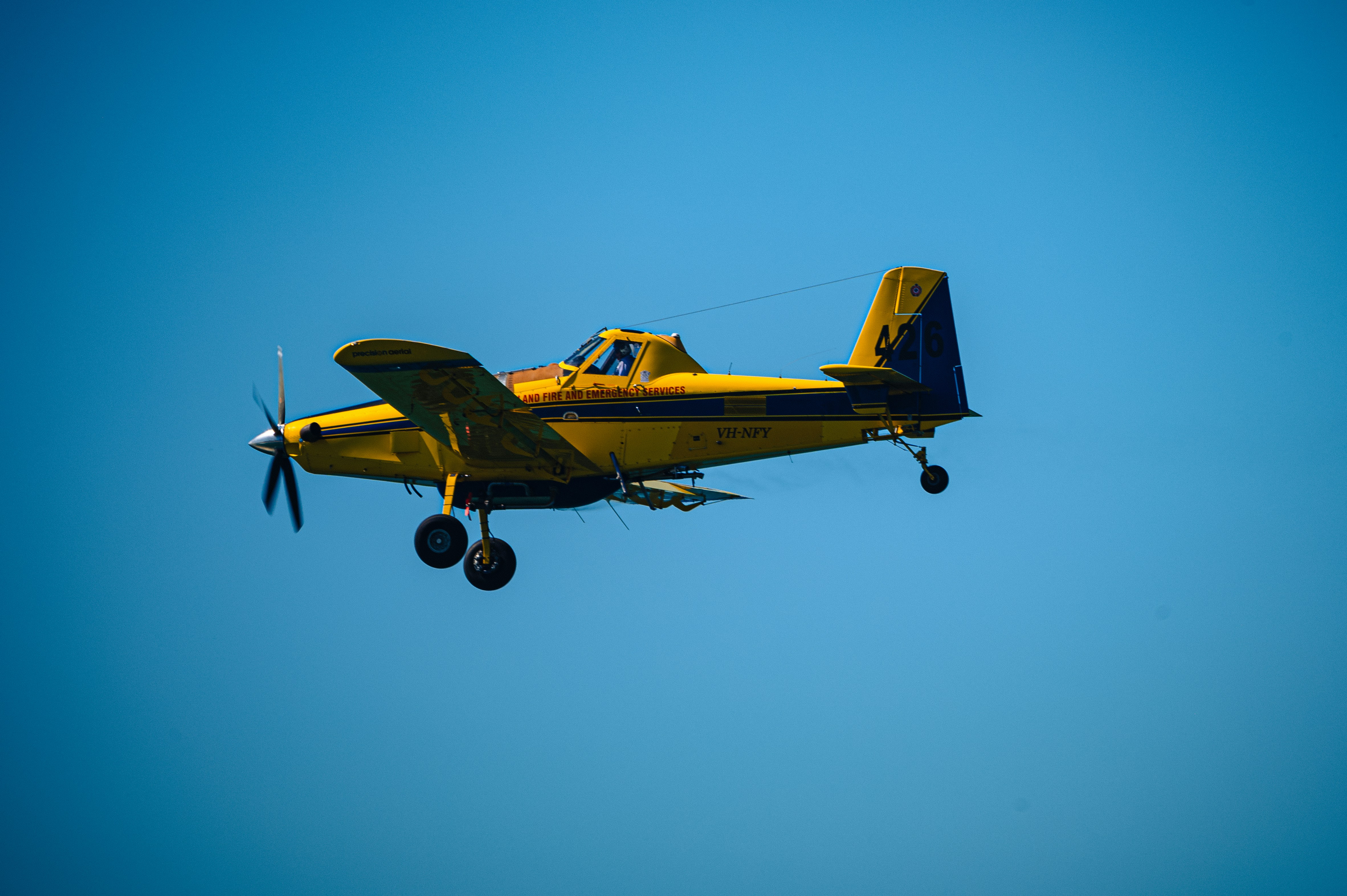 A small yellow airplane flying through a blue sky