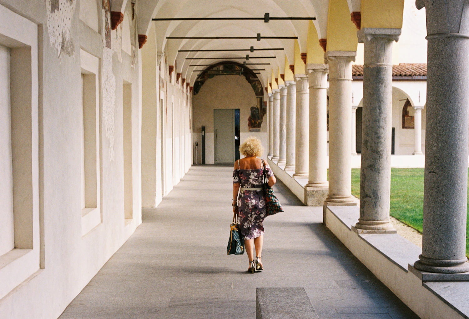 A figure walking away down a long arcaded portico in morning light