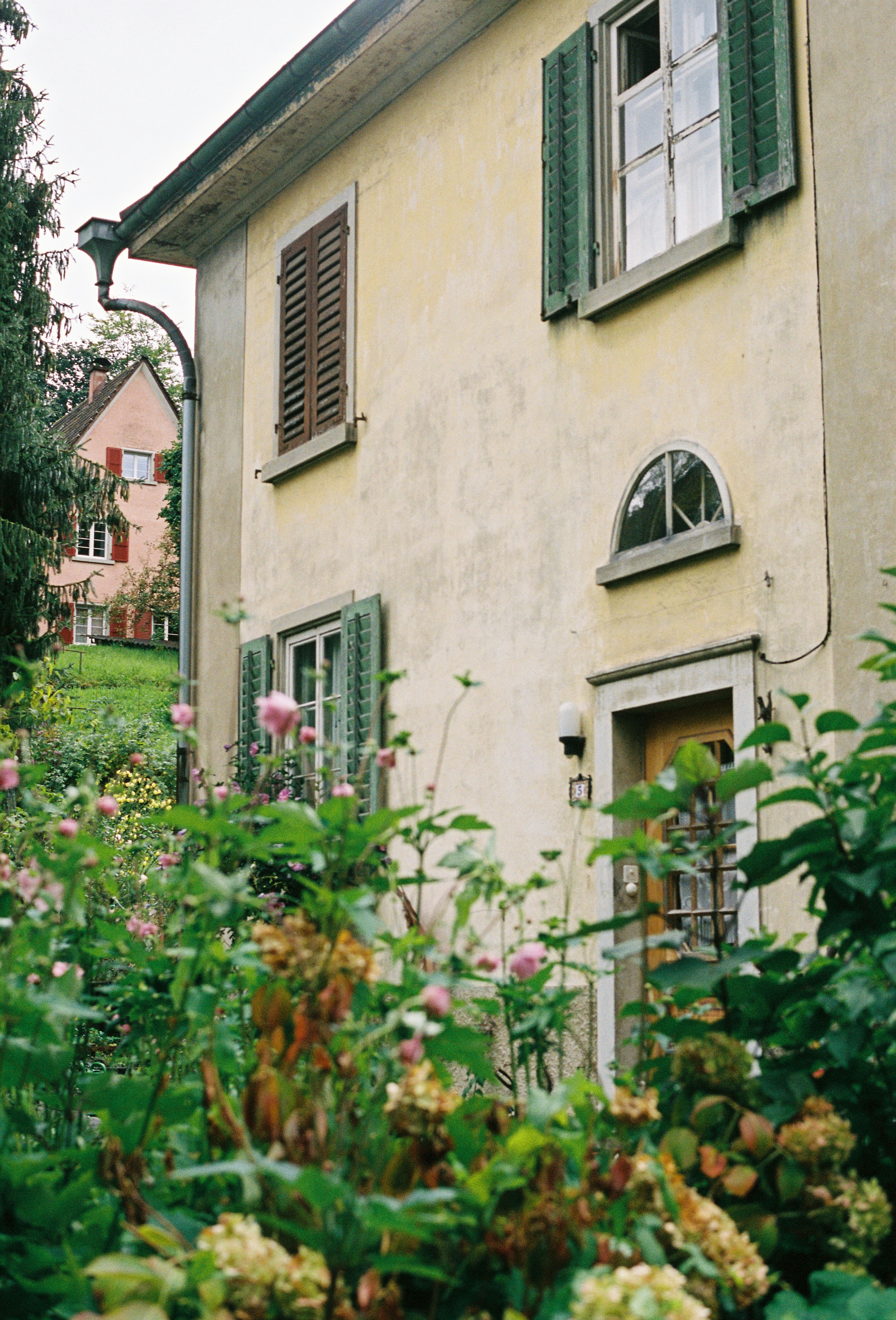 A house with green shutters and flowers in front of it