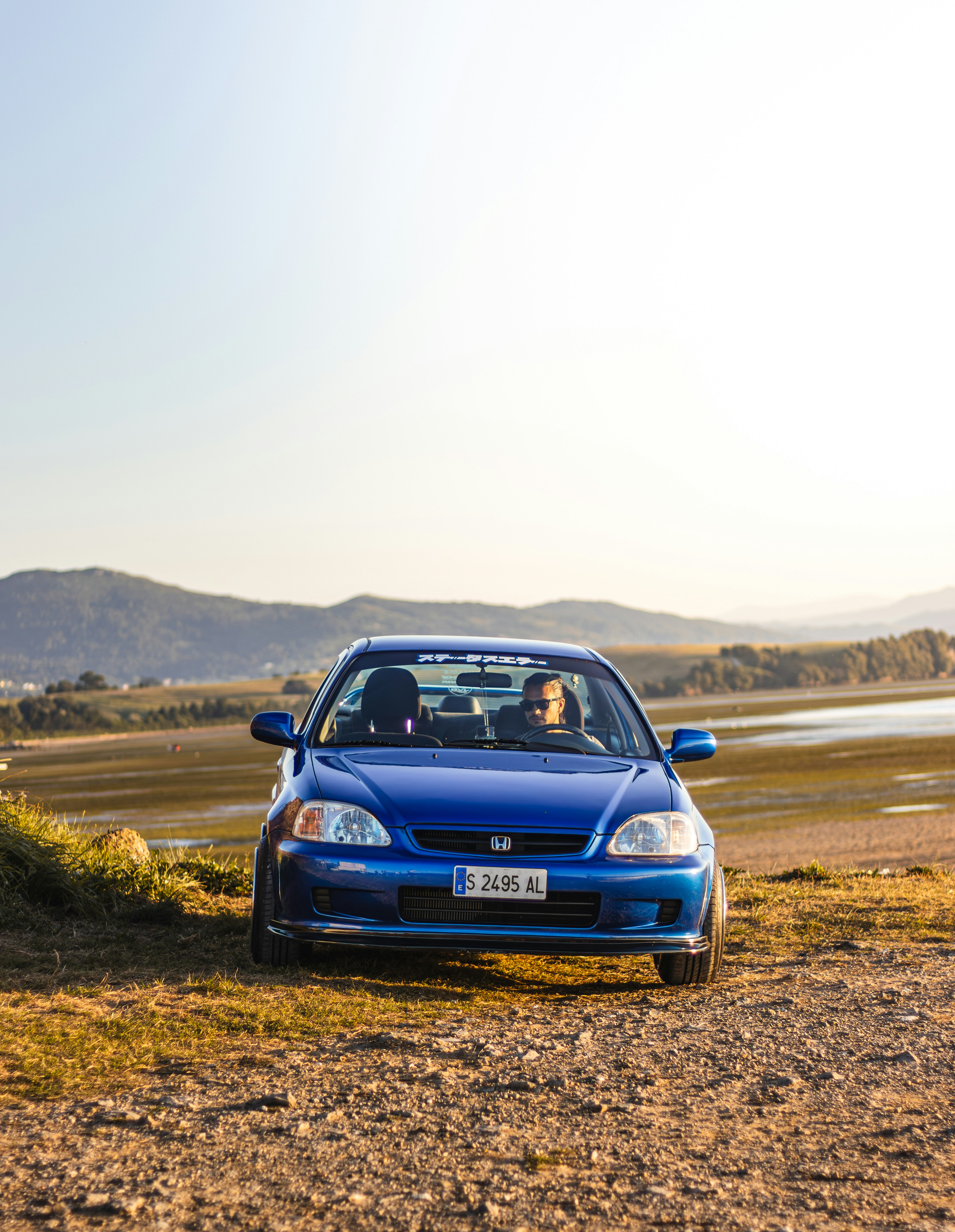 A blue car parked on the side of a dirt road