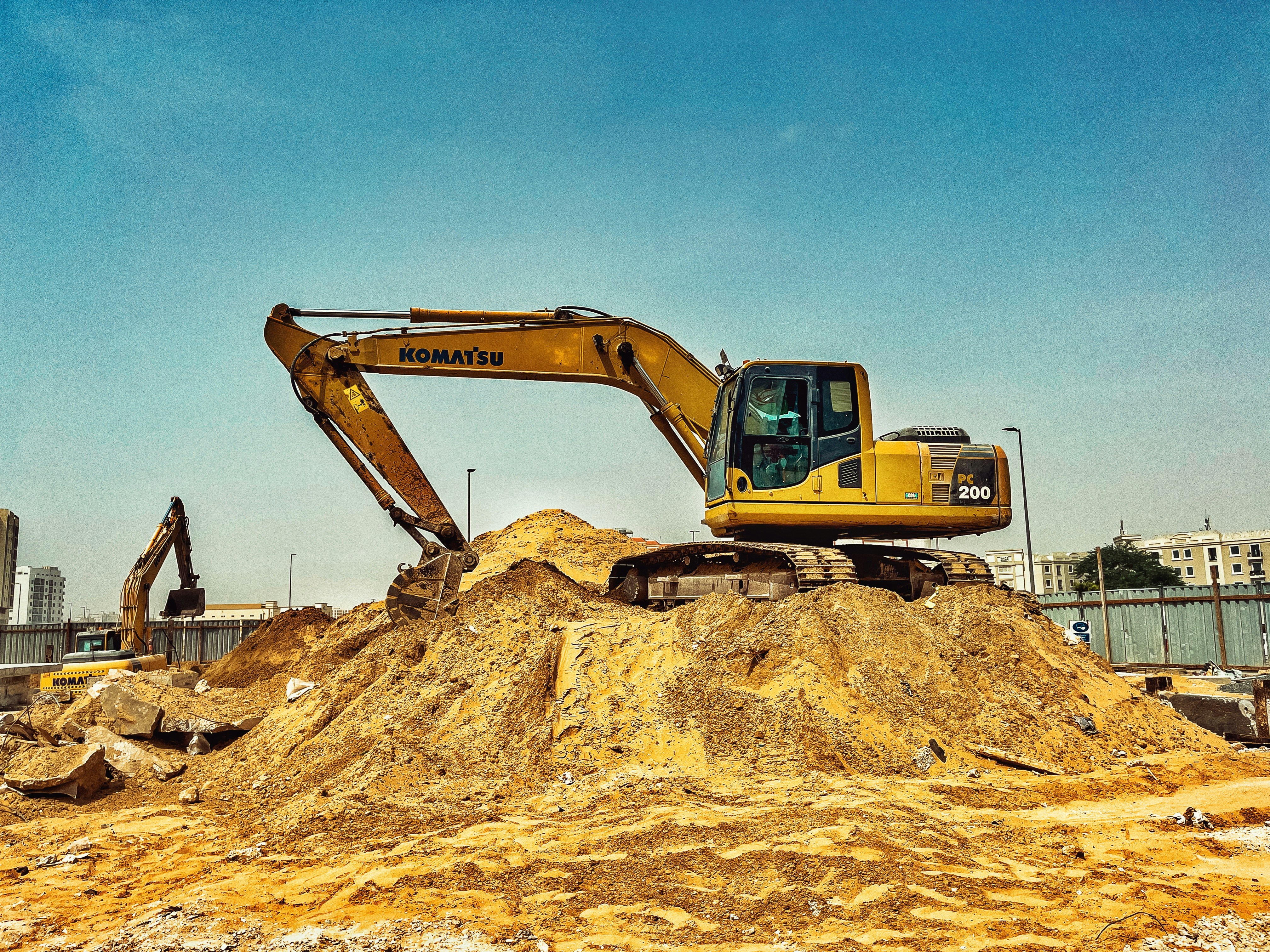 Large yellow hydraulic excavator on a construction site with dirt mounds and clear sky