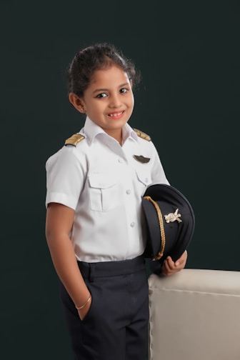 A little girl in a uniform holding a hat