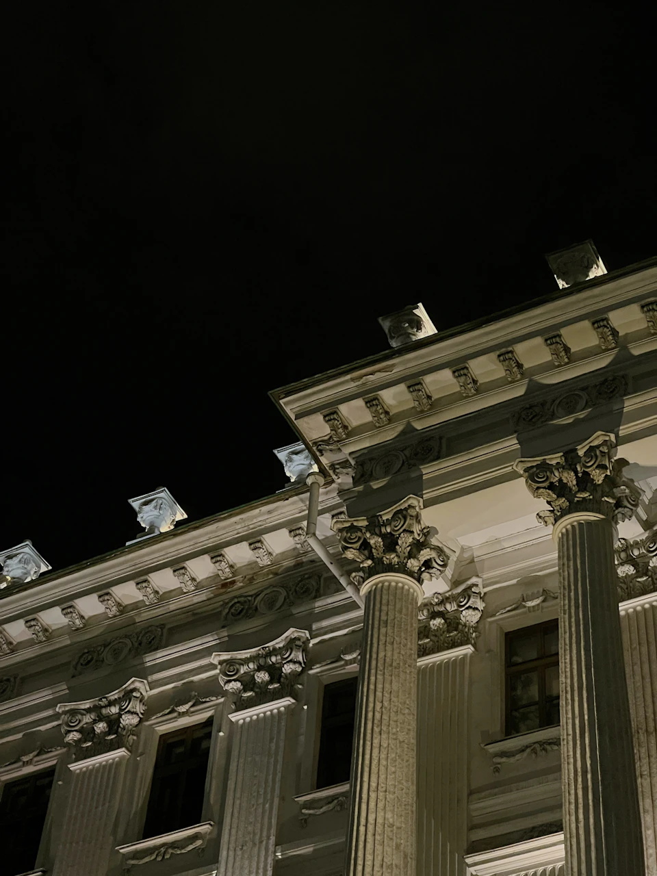 The image depicts a majestic white building with three towering columns, each adorned with intricate carvings and statues on either side. The building is illuminated by numerous lights that cast a warm glow against the dark night sky. The perspective of the photo is from below, looking up at the imposing structure, emphasizing its grandeur and architectural beauty.

The image also contains some text in the top left corner, but it is not clear what it says without additional context or information about the content.