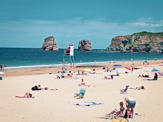A crowded beach with people sitting and standing in the sand