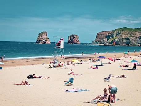 A crowded beach with people sitting and standing in the sand