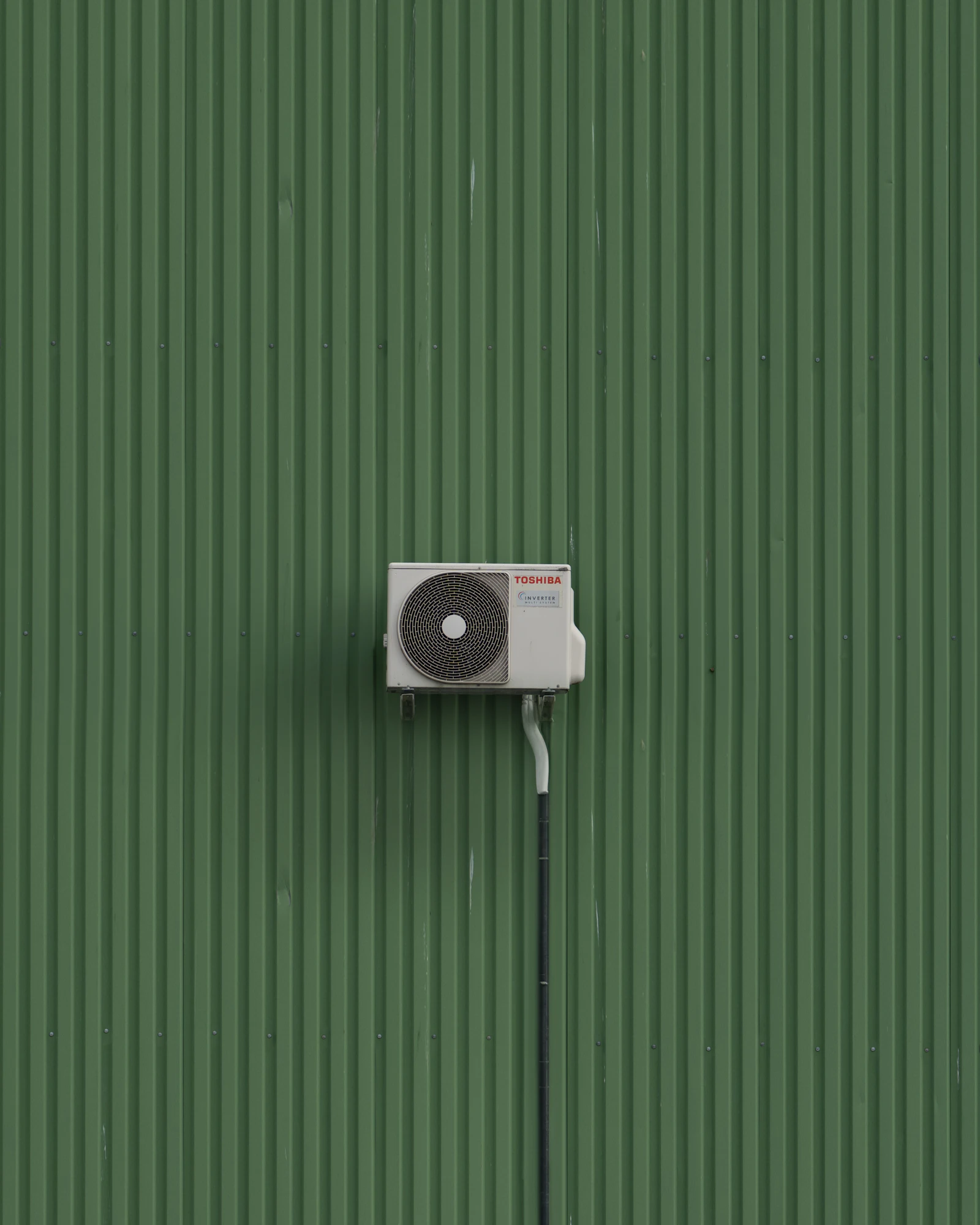White outdoor condenser mounted on green corrugated metal siding
