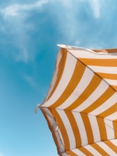 An orange and white striped umbrella against a blue sky