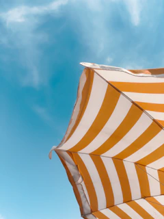 An orange and white striped umbrella against a blue sky