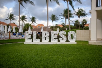 A sign that says el beso in front of some palm trees