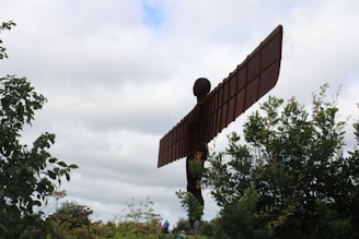 A large metal angel statue sitting in the middle of a forest