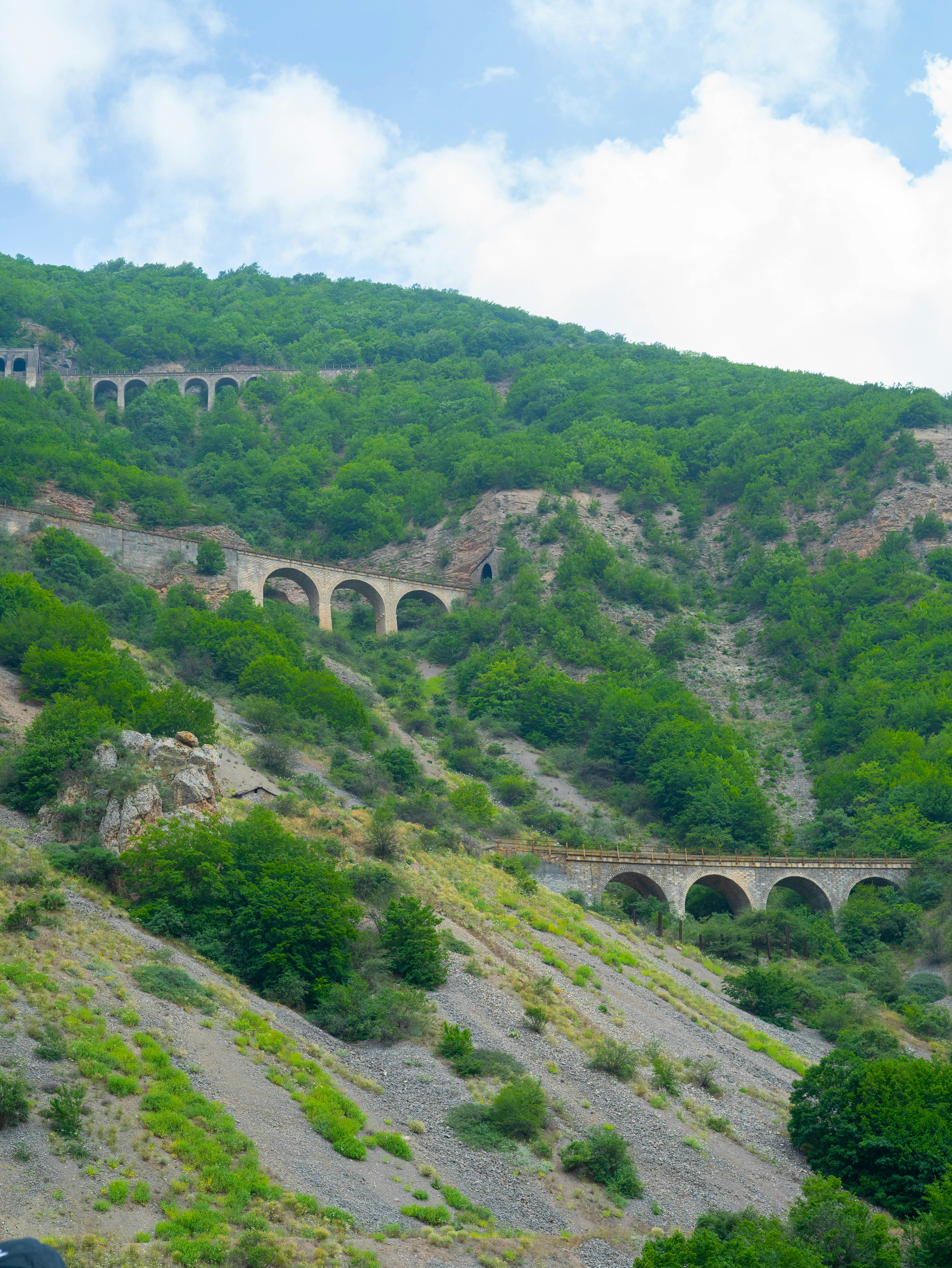A train traveling down a train track next to a lush green hillside