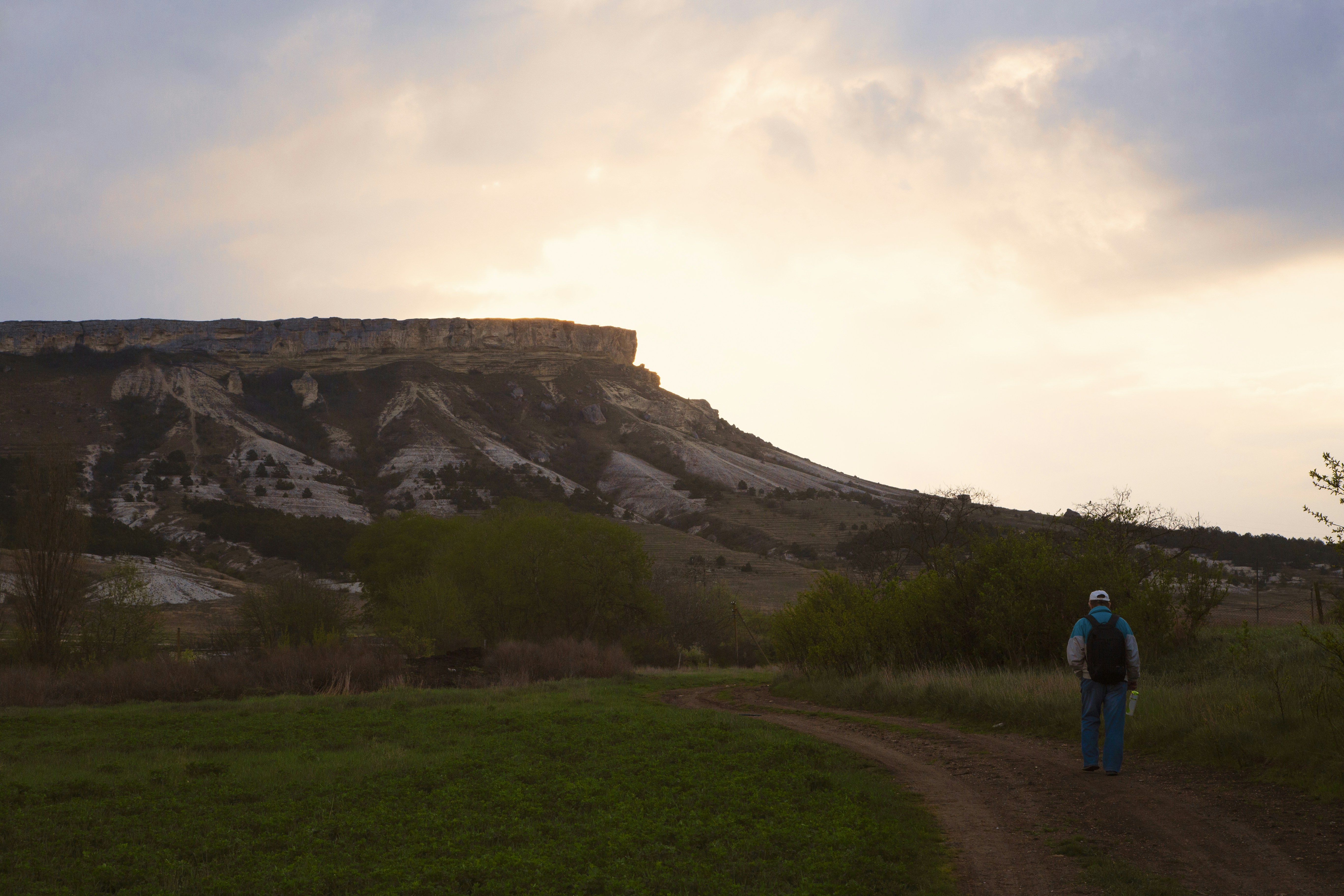 A person walking down a dirt road in front of a mountain