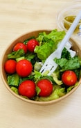 A wooden table with a bowl of salad and a plastic fork