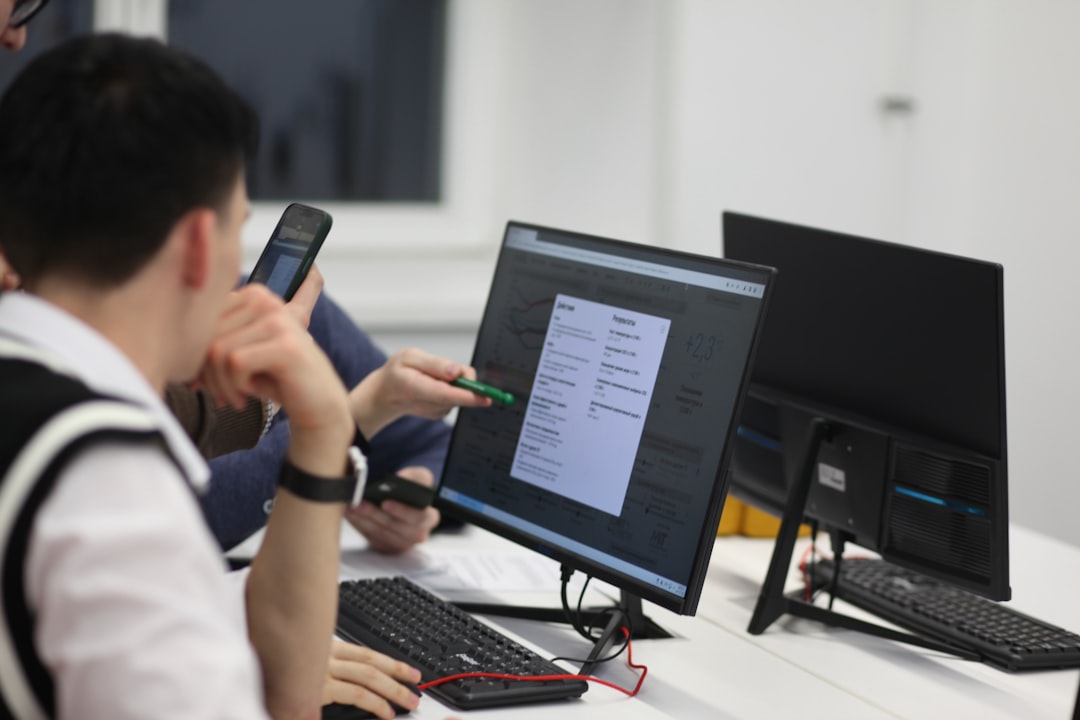 A group of people sitting at a table with computers, A group of students sitting in front of a monitor representing some climate change statistics. One is pointing at the screen with a pen.