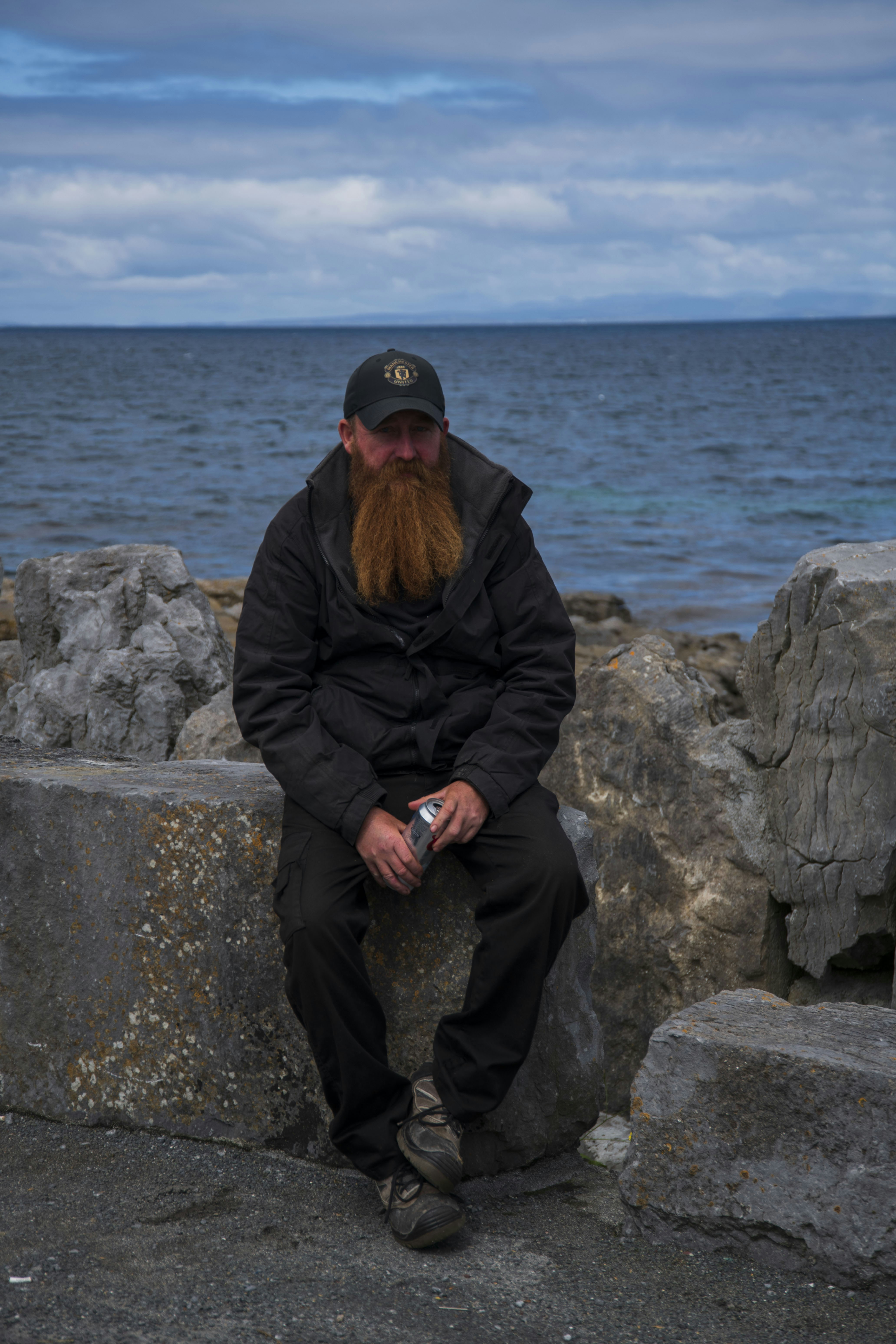 A man with a red beard sitting on a rock near the ocean