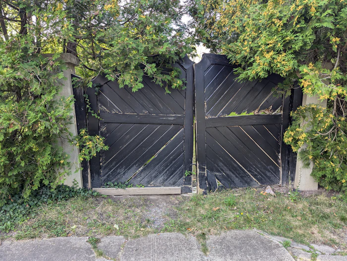 Black wooden double gate framed by green trees
