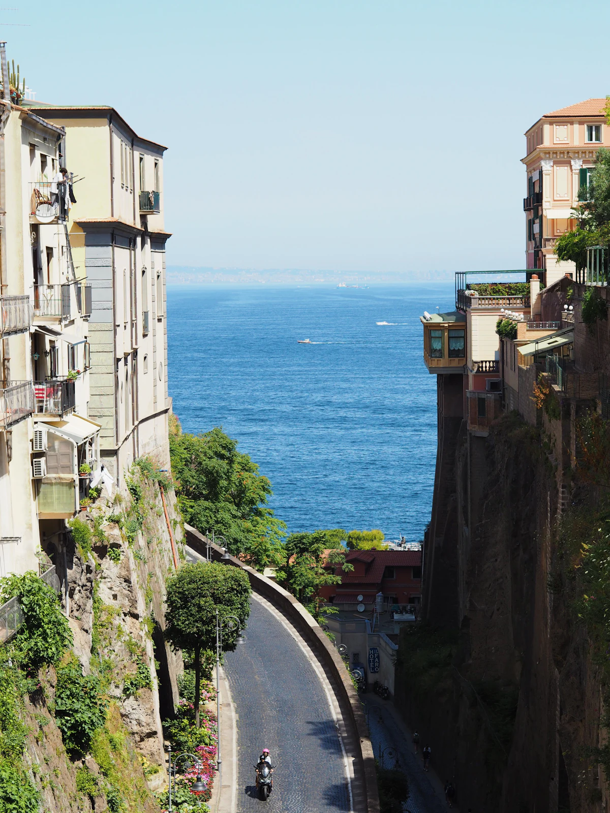 A motorcycle driving down a narrow, winding cliffside road along the Italian coast