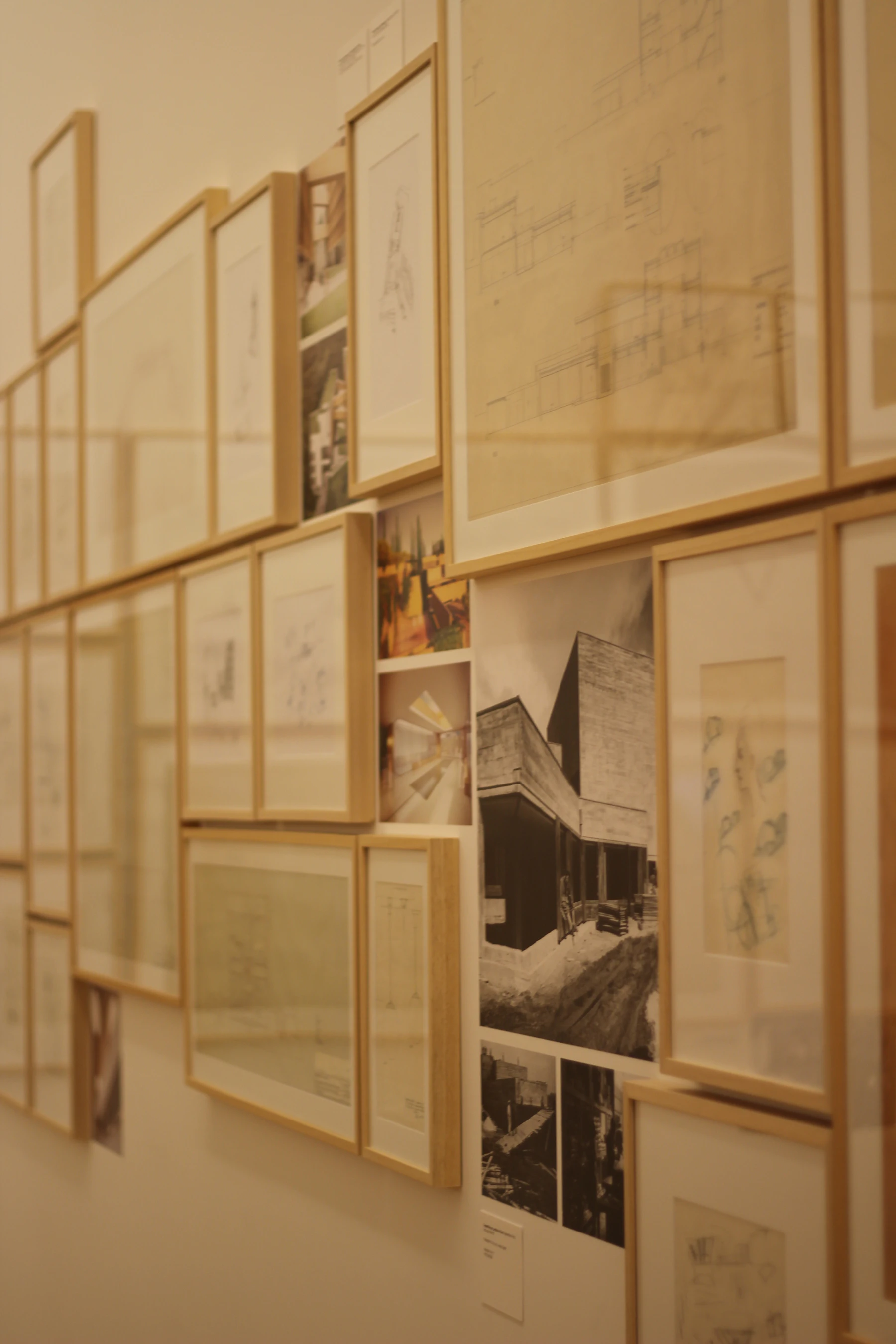 Drawings and photographs in pale wood frames hung close together on a wall