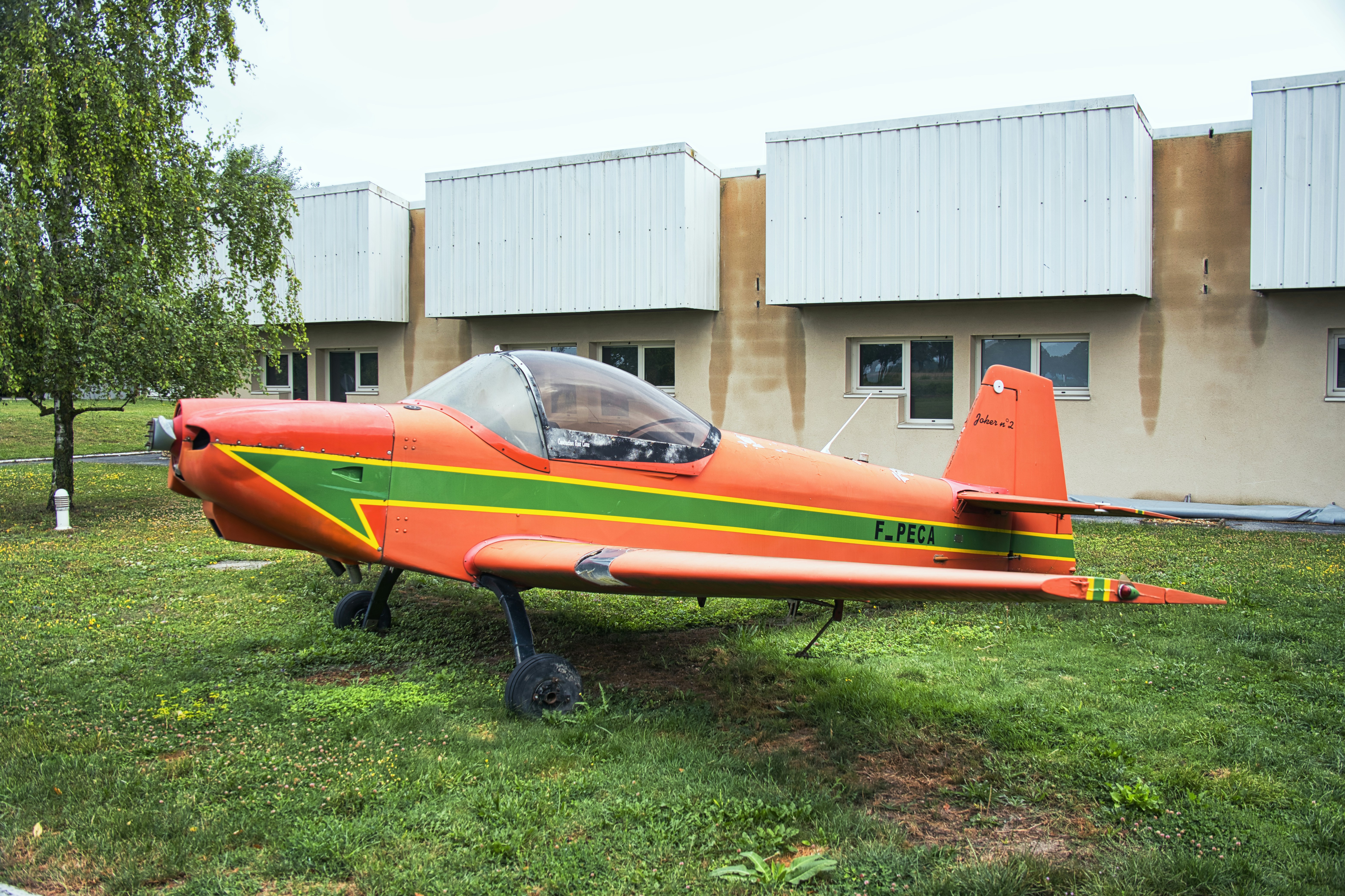Un avión naranja y verde sentado en la cima de un exuberante campo verde