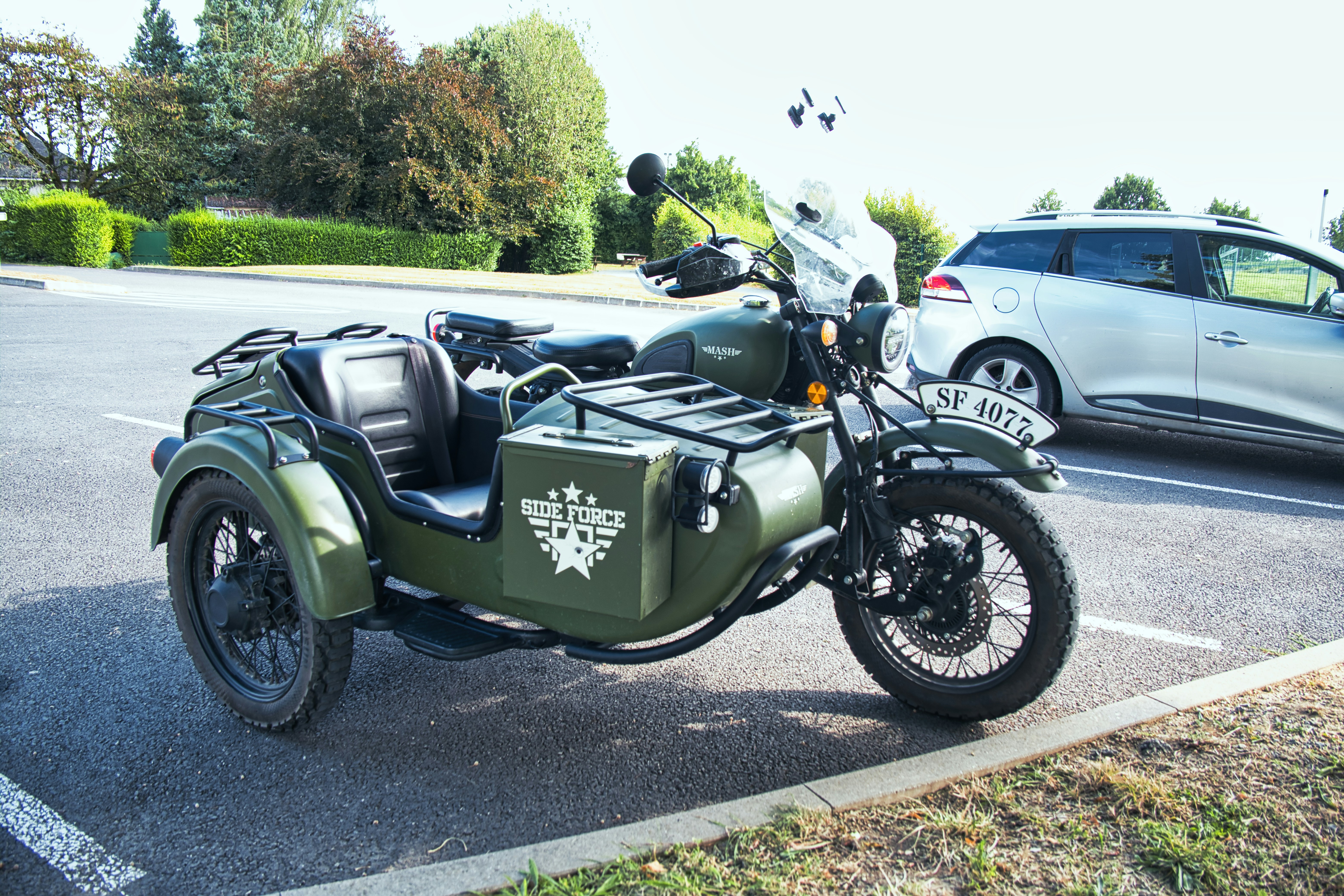 Une moto verte garée sur un parking à côté d’une voiture