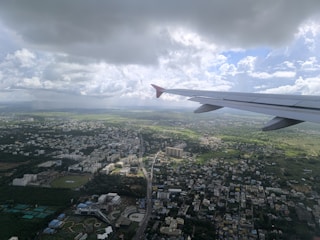 An airplane wing flying over a city under a cloudy sky