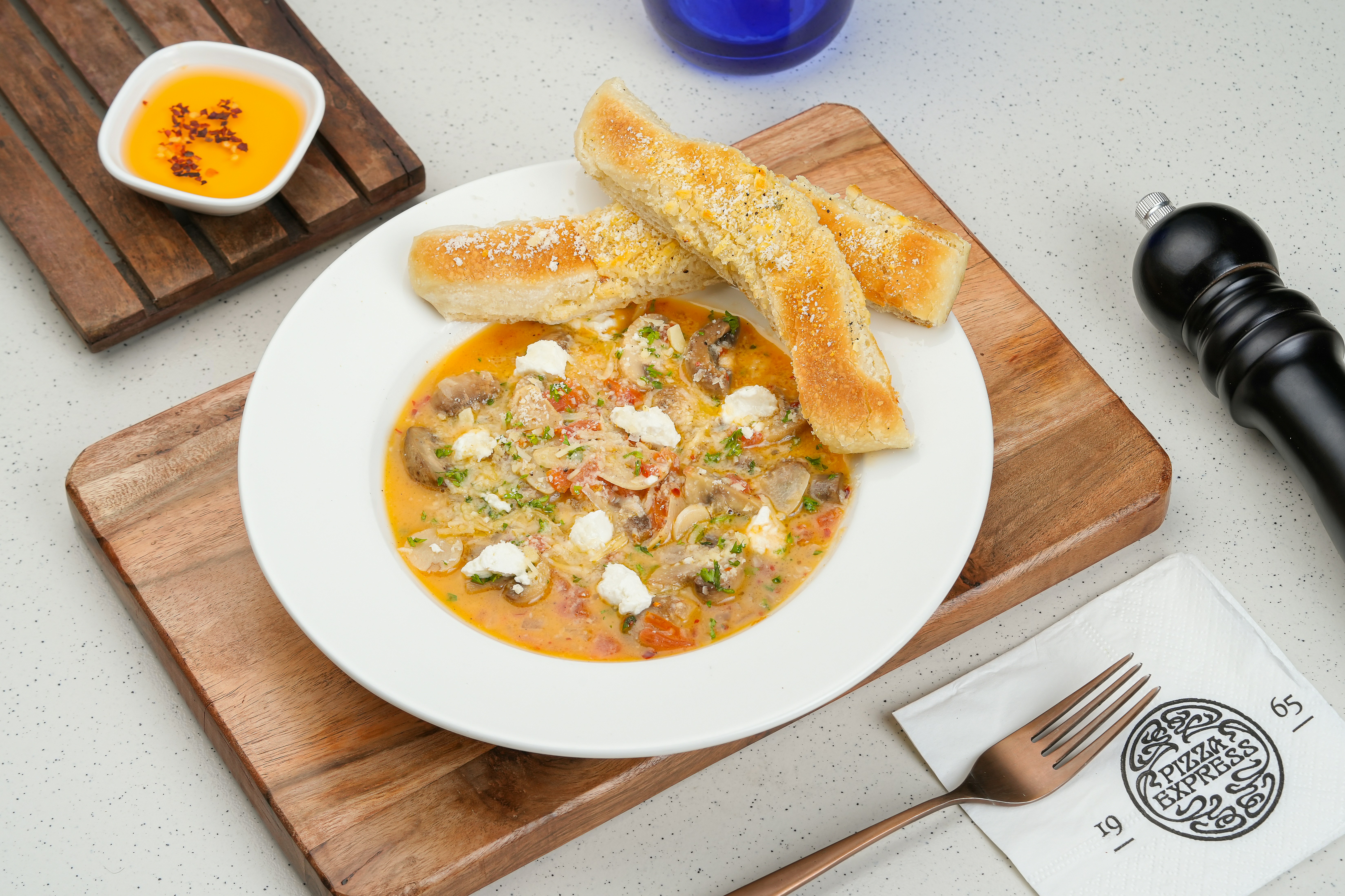 A bowl of soup on a cutting board next to a knife and fork