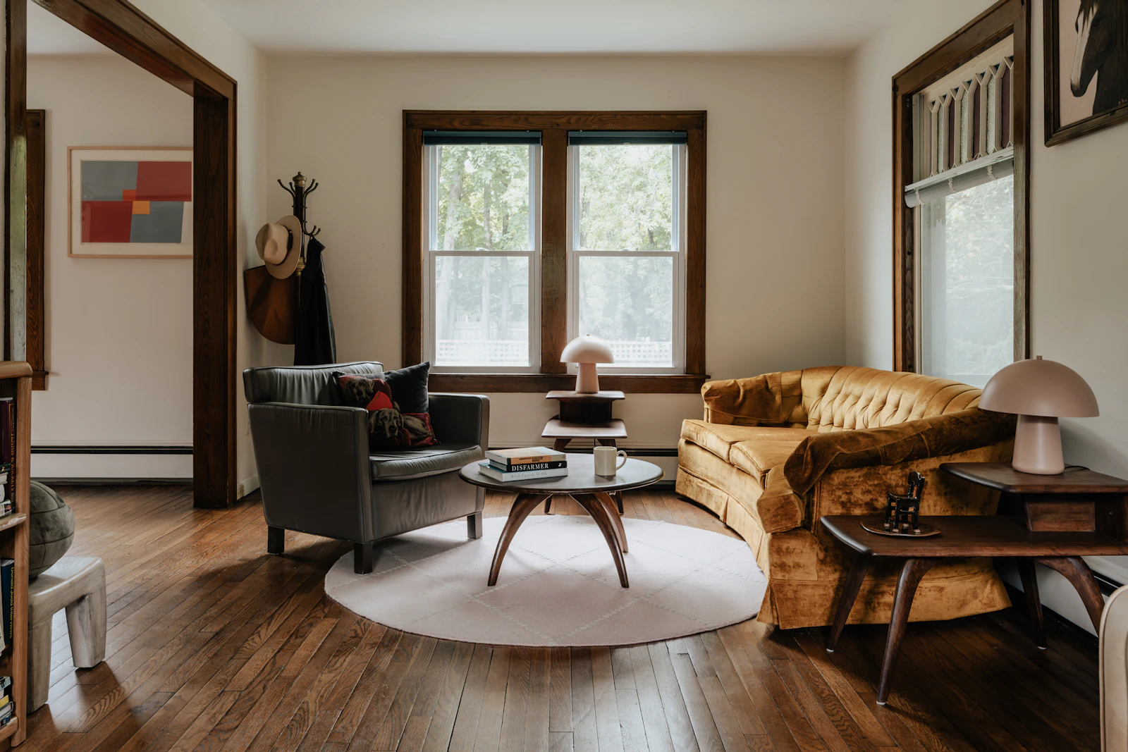 A relatable living room with warm wood floors, upholstered seating, windows, and everyday furniture.