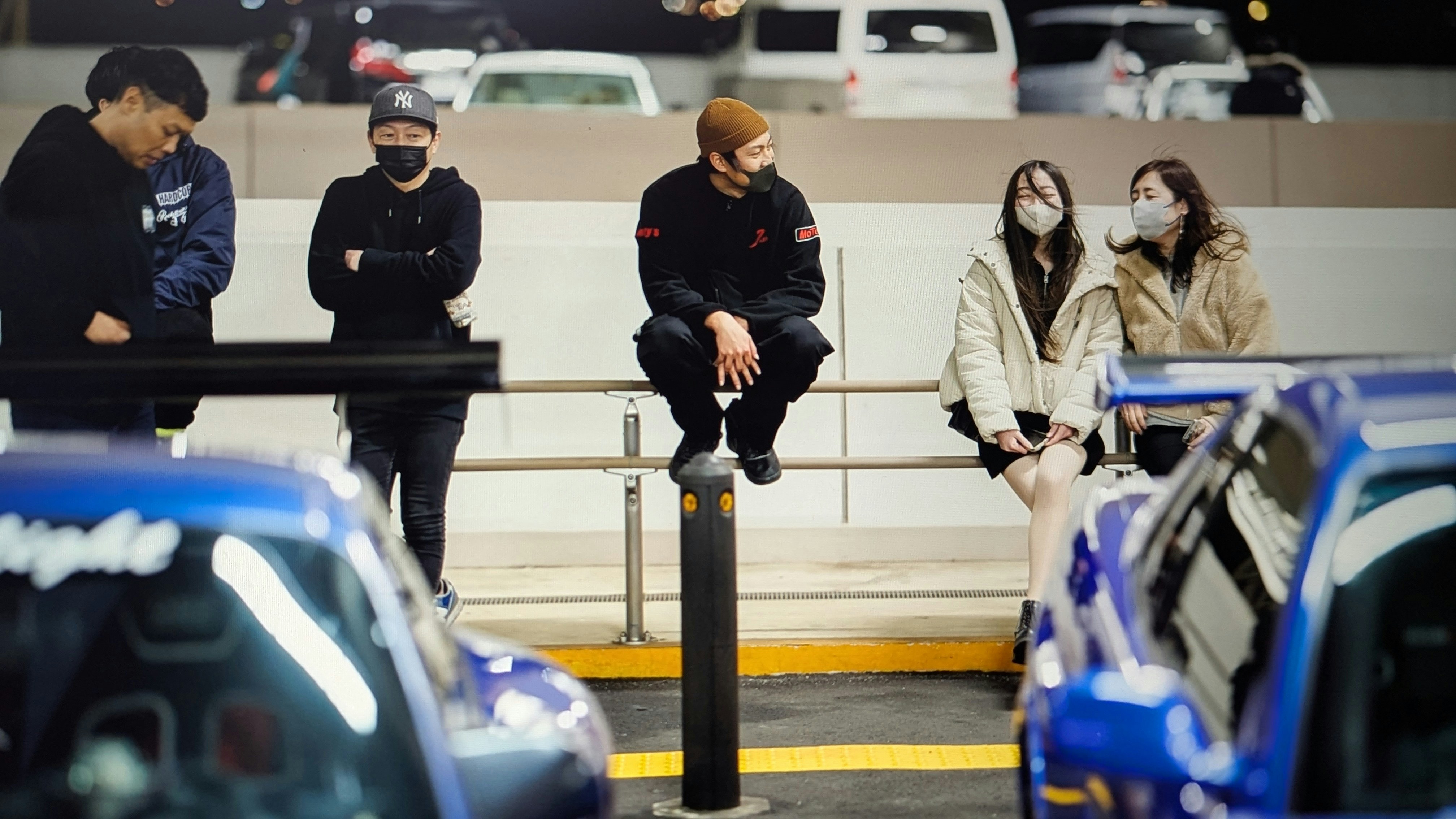 A group of people sitting on a bench in a parking lot