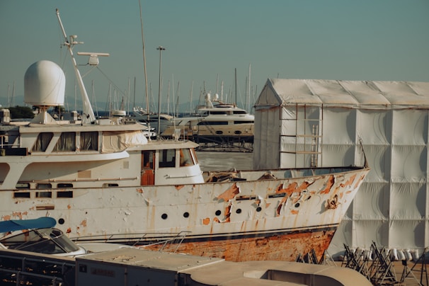 A rusted boat sits in a harbor next to a building