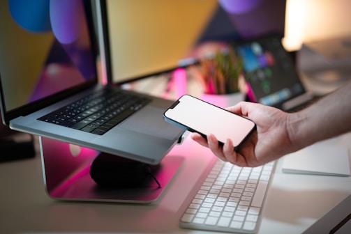 A person holding a cell phone next to a laptop