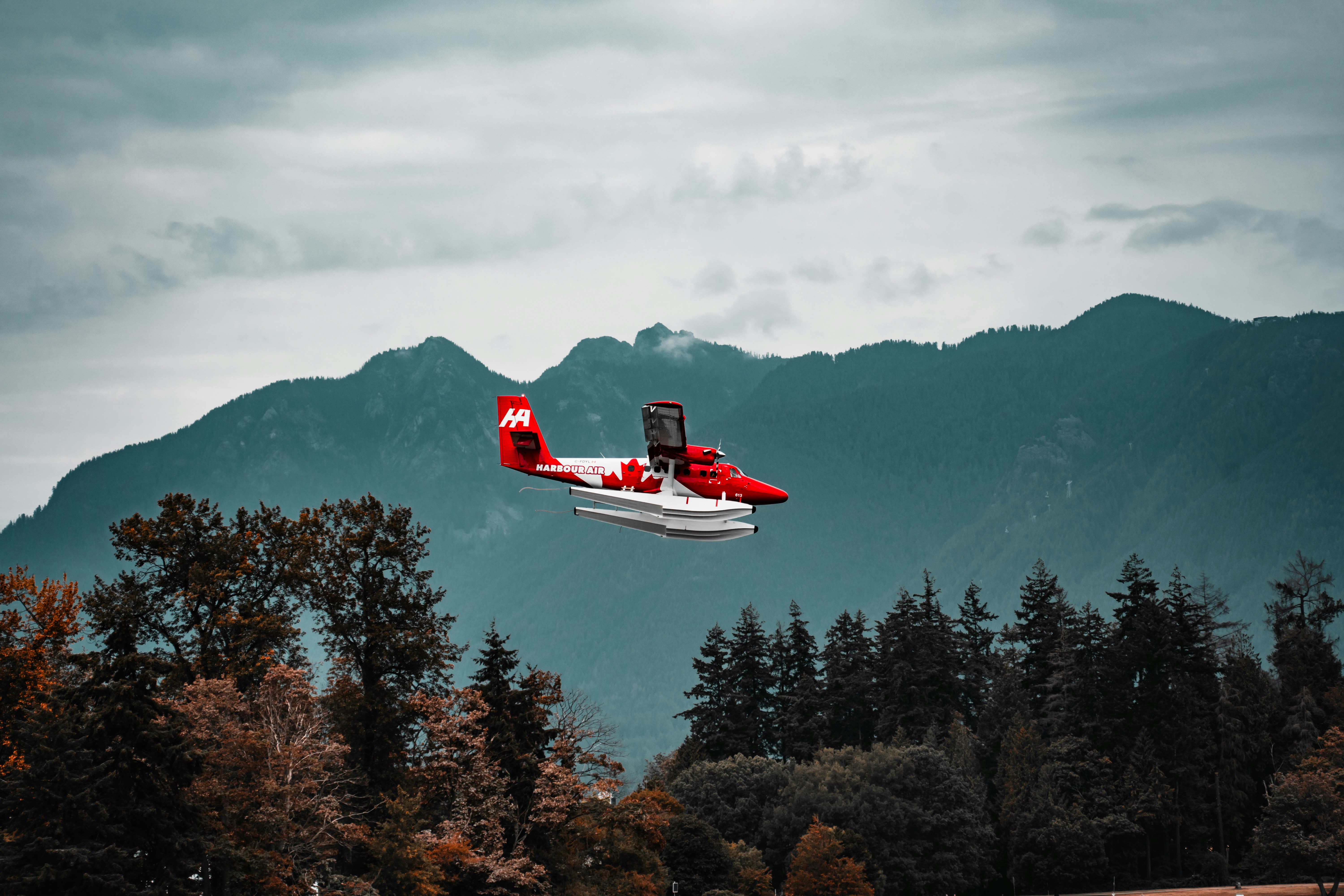 A red and white plane flying over a forest, 
