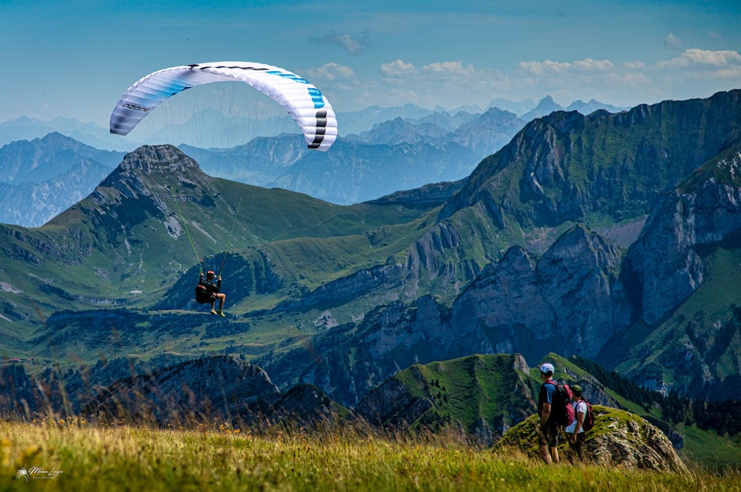 Two people are paragliding over a mountain range,