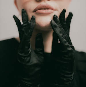 A woman wearing black gloves with her hands on her face