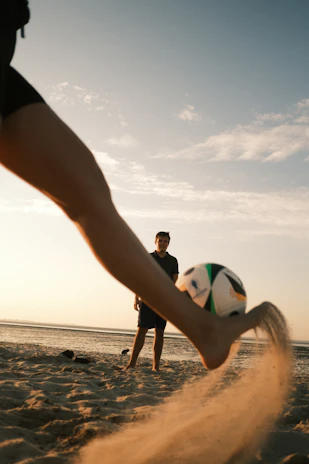 A person kicking a soccer ball on a beach