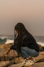 A woman sitting on top of a rock next to the ocean