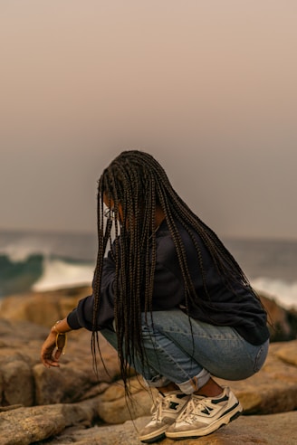 A woman sitting on top of a rock next to the ocean