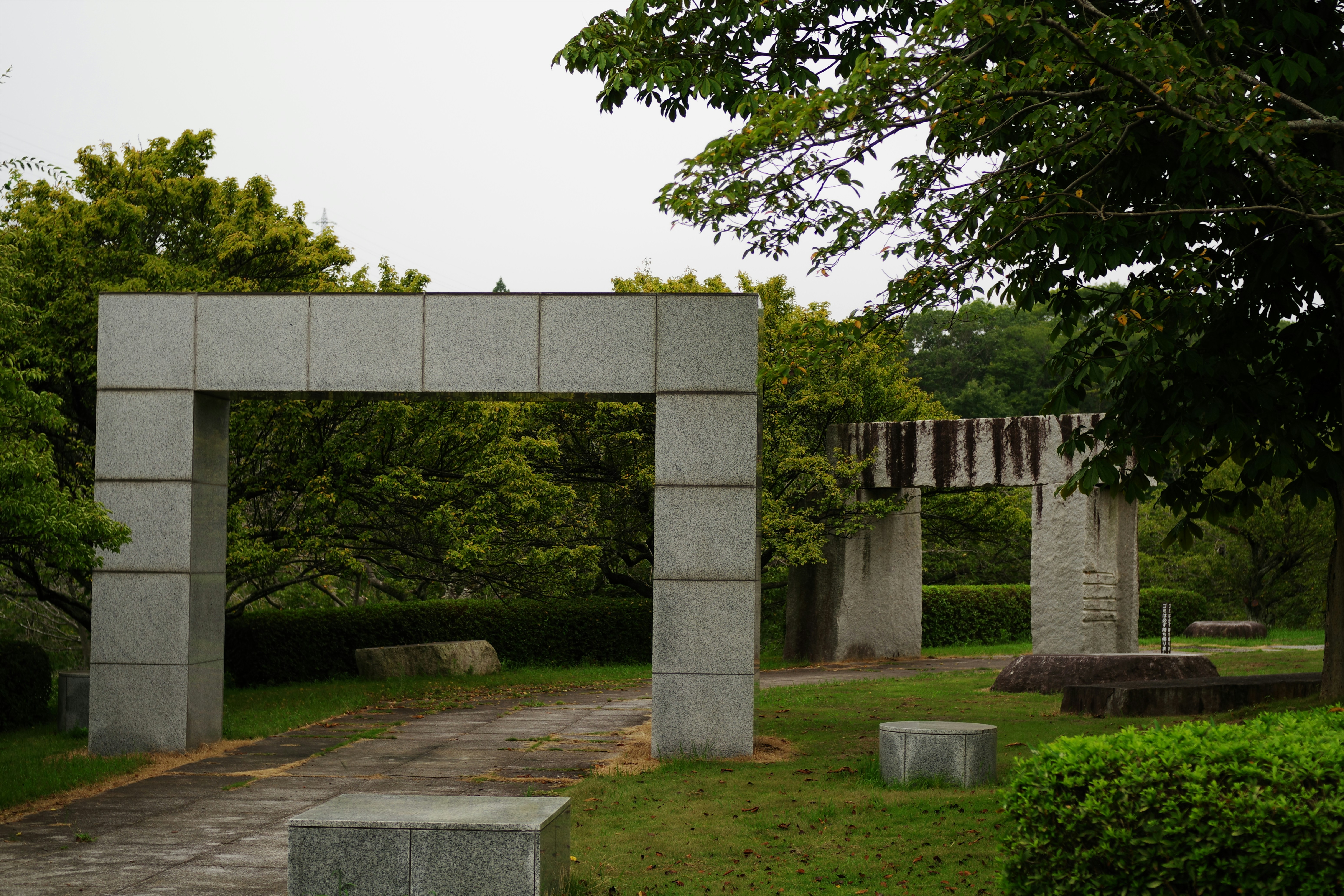 A stone arch in a park with a bench and trees