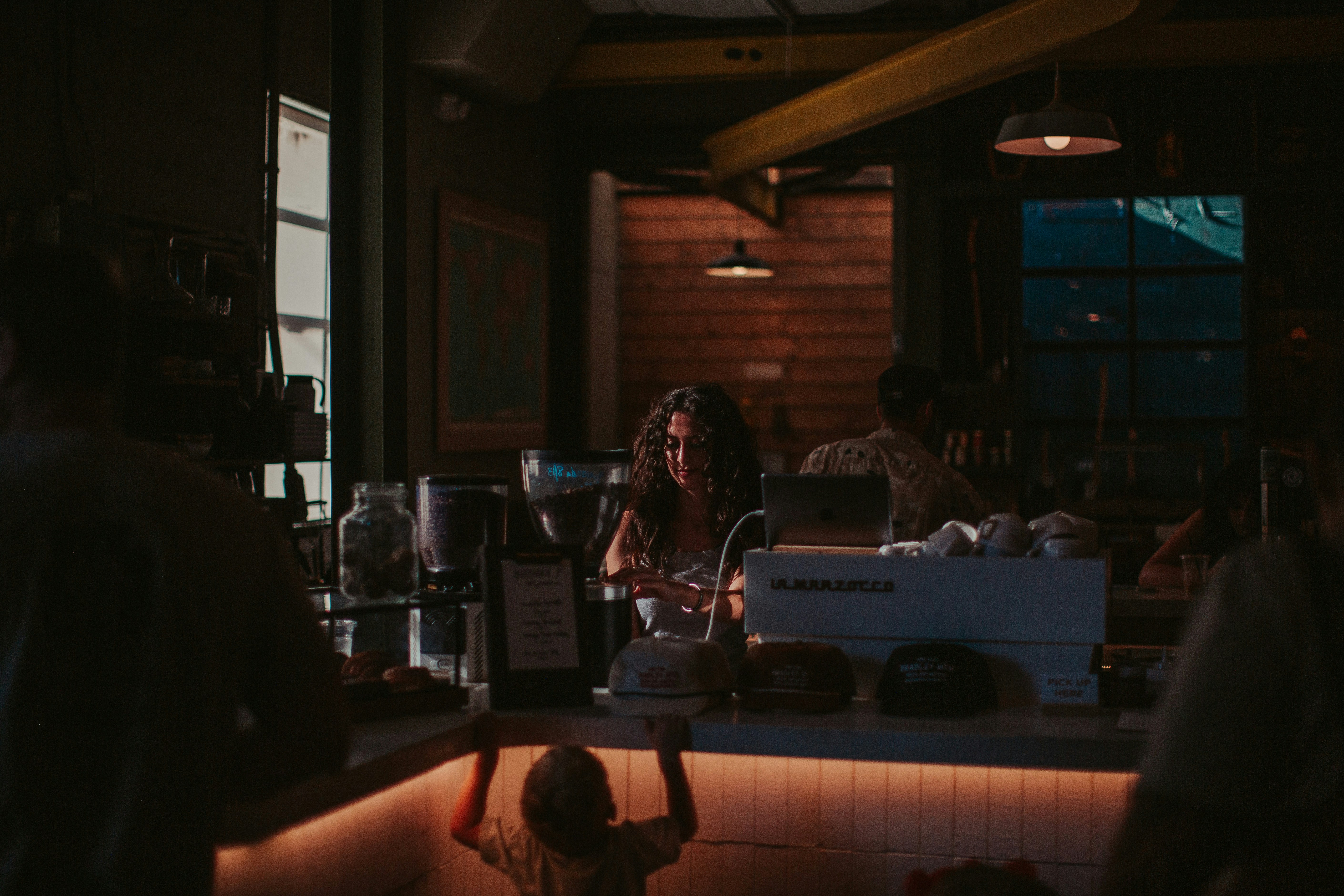 barista pouring latte art under warm amber pendant light in dark modern cafe at night