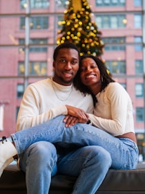 A man and woman sitting on a couch in front of a christmas tree